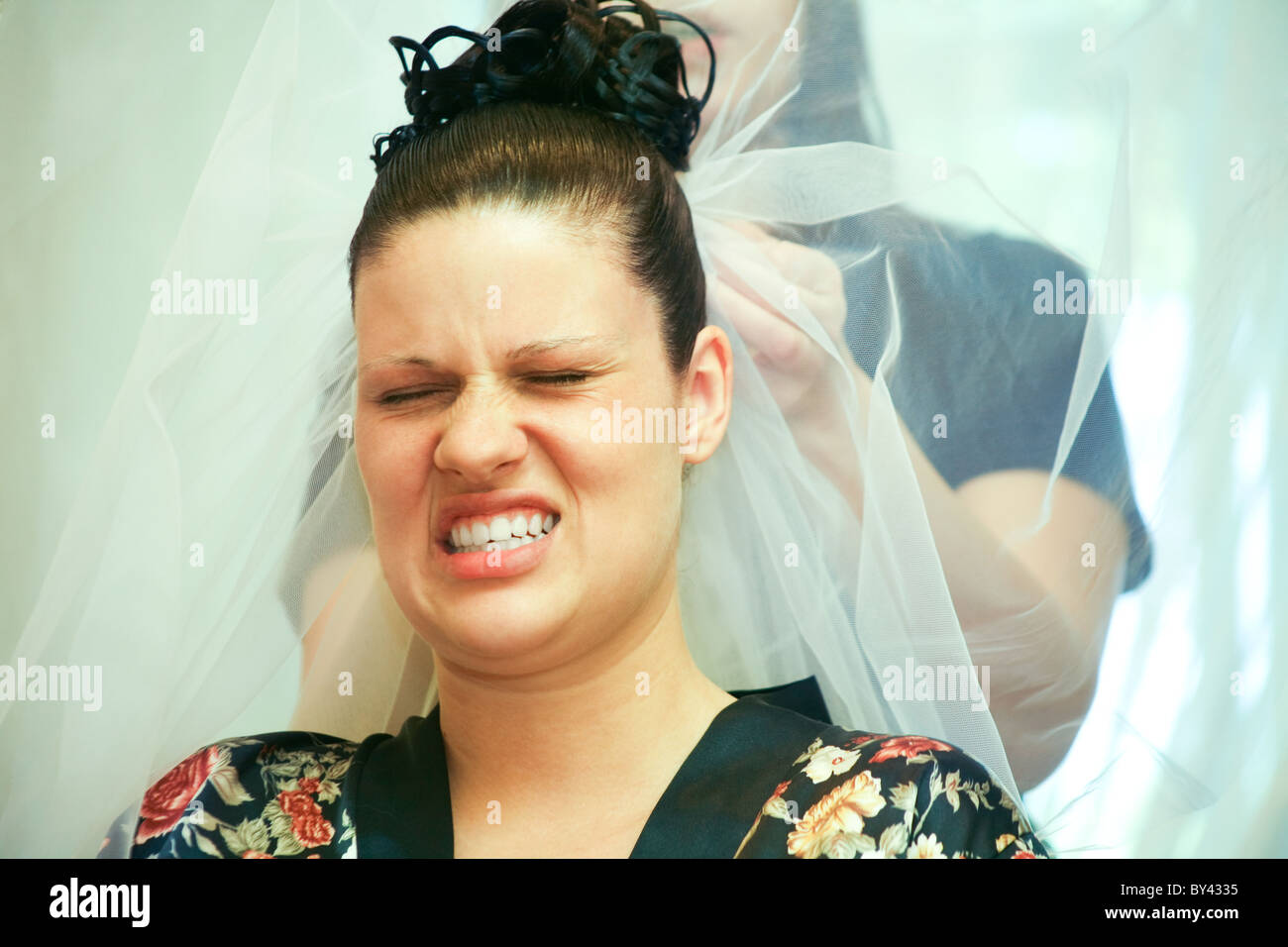 Gesicht der jungen Frau, die Schmerz auszudrücken, während ihr Haar für Hochzeit durchgeführt wird Stockfoto