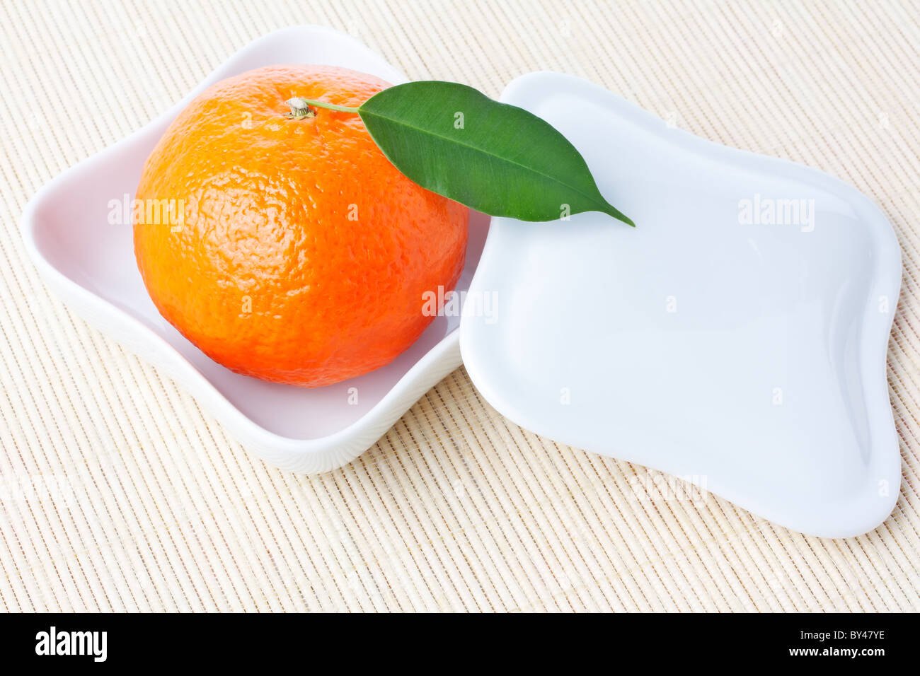 Reife frische Orange Mandarine mit grünen Blatt auf weiß geformte Platte mit Deckel Stockfoto