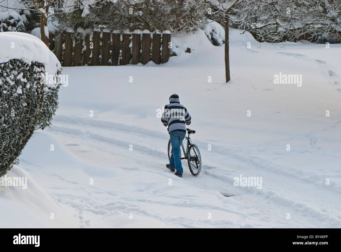 Gefrorene Großbritannien Lone schiebt Radfahrer Fahrrad durch verschneite Straßen Warlingham Surrey, England UK. Stockfoto