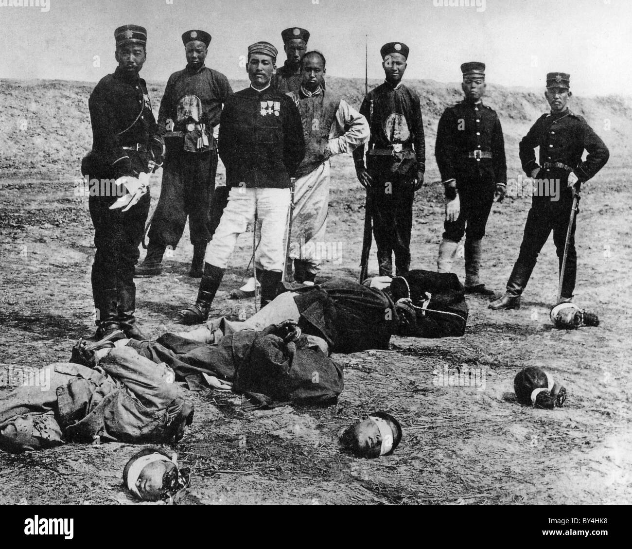 BOXERAUFSTAND chinesischer Henker mit ihren Opfern in einem 1900 Foto mit japanischen Soldaten im Hintergrund Stockfoto