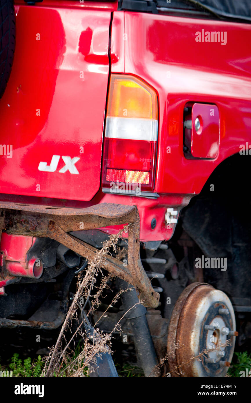 Ein rot JX-Fahrzeug mit einem gestohlenen Rad und Nabe verwüstet und in einem Schrottplatz bereit zerdrückt werden Stockfoto