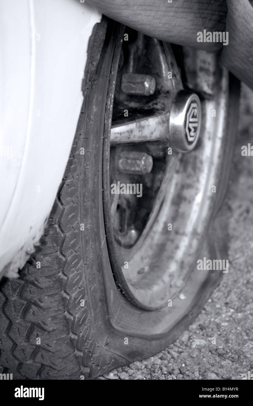 Ein platter Reifen auf einem alten MG Auto im schwarzen und weißen Monochrom abgebaut Stockfoto