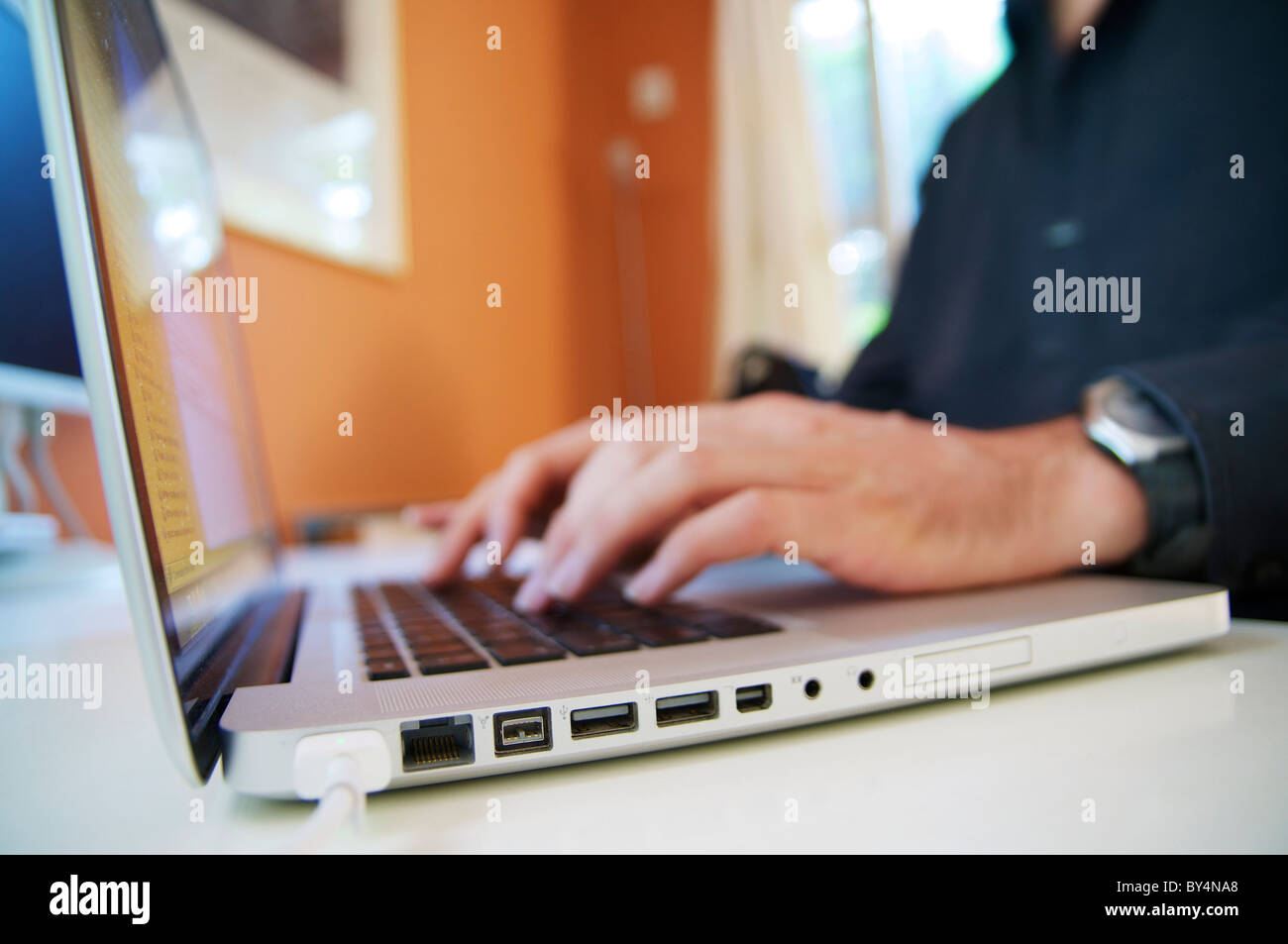 Mann sitzt hinter einem Laptop am Schreibtisch einen Text schreiben. Stockfoto
