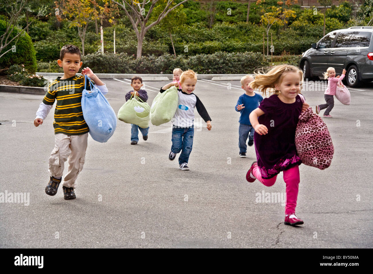 Eifrige Kinder durchlaufen einen Parkplatz zu ihrer s Southern California-Vorschule. Beachten Sie die Ruhezeit Schlafsäcke. MODELL Stockfoto