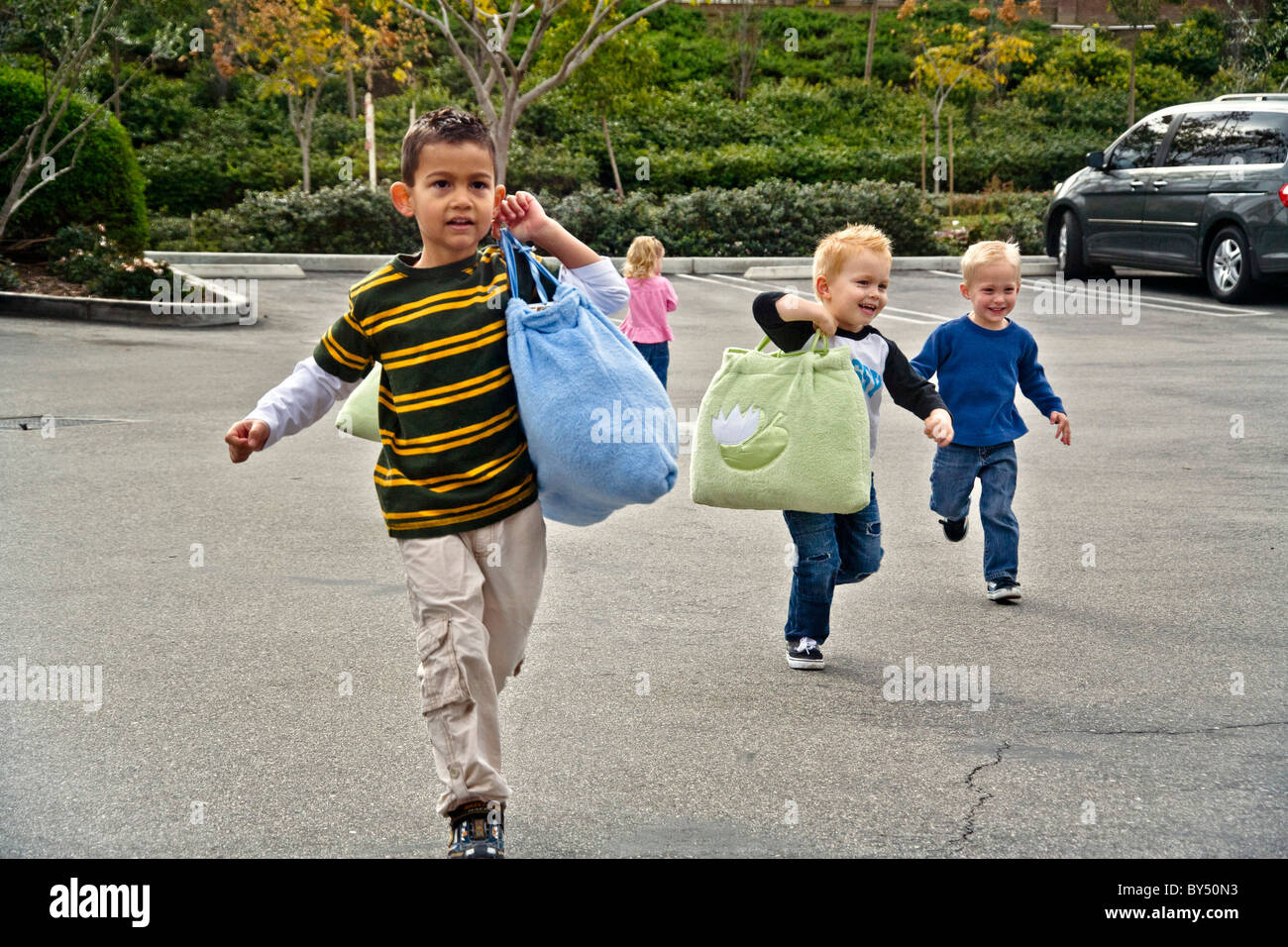 Eifrige Kinder durchlaufen einen Parkplatz zu ihrer s Southern California-Vorschule. Beachten Sie die Ruhezeit Schlafsäcke. MODELL Stockfoto