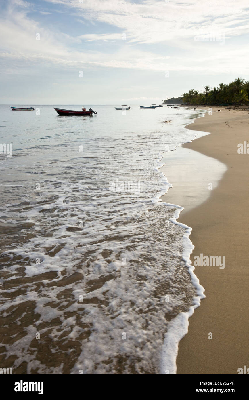 Bei Sonnenaufgang, Costa Rica waschen Wellen gegen das Ufer der ganz Angeln Stadt Manzanillo. Stockfoto
