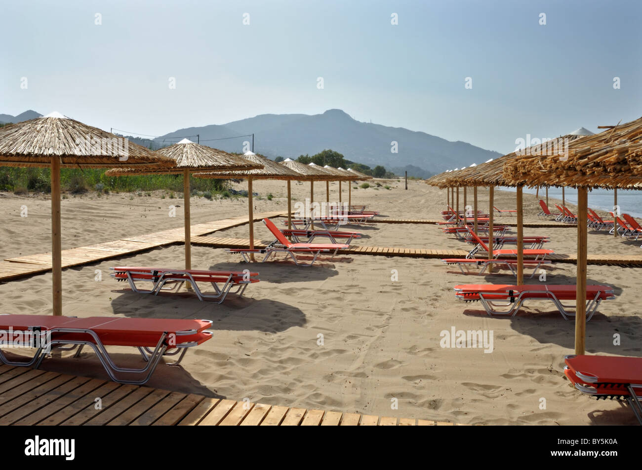 Stroh Sonnenschirme und Stuhlreihen Lounge Sonnenliege am Sandstrand in Griechenland. Stockfoto