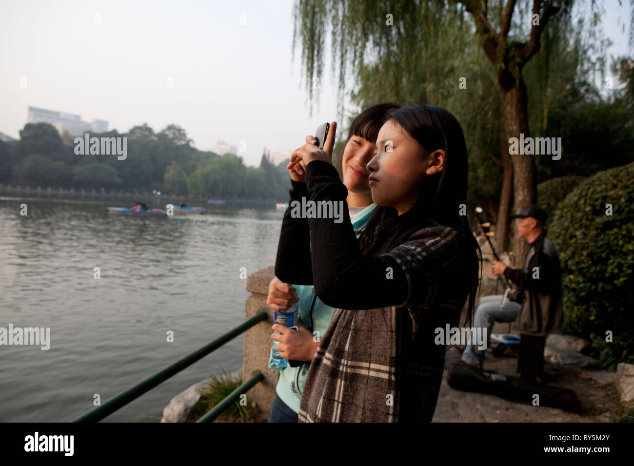 Mädchen im Teenageralter fotografieren neben See in Luxon Park, Shanghai, China Stockfoto
