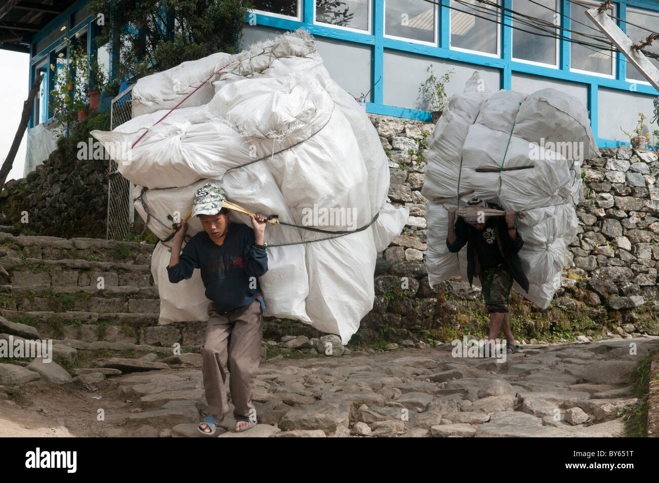 junge Porter mit eine riesige Ladung in Lukla Dorf in der Everest Region von Nepal Stockfoto