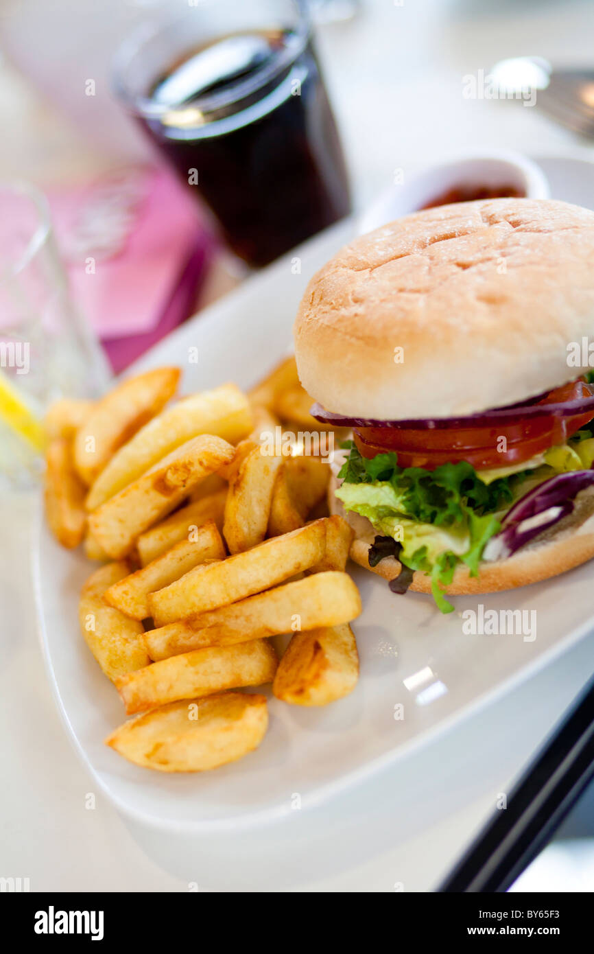 Ein Teller mit Burger und Pommes frites sitzt auf einer Café-Tisch zusammen mit einem Cola-Getränk. Stockfoto