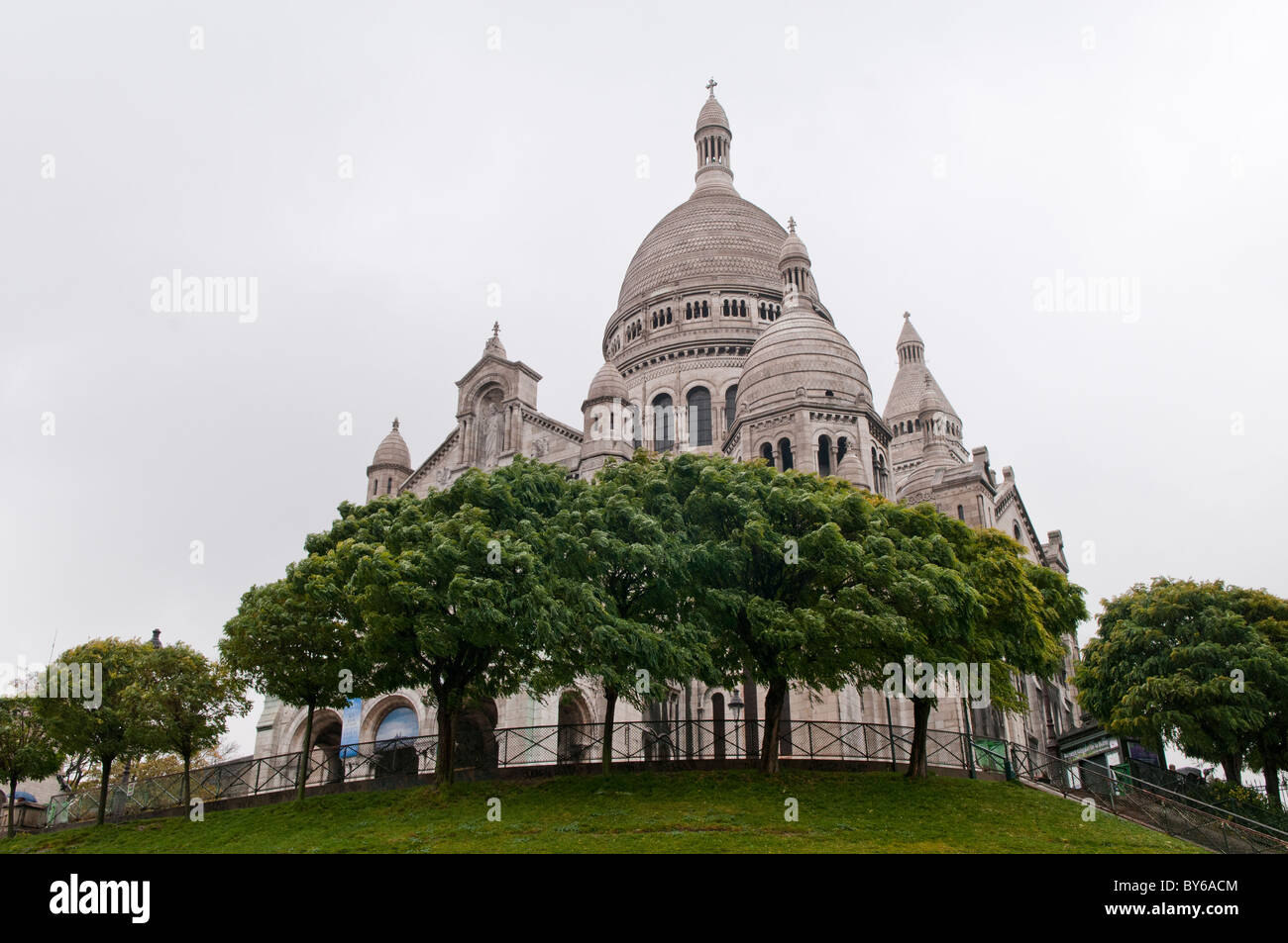 Sacré-Cœur-Basilika Weißer Kuppel-Außenbereich Montmartre Paris Frankreich | PARIS, Frankreich — Von den Rasenflächen des Square Louise-Michel aus gesehen, krönen die zentrale Kuppel und der Glockenturm der Sacré-Cœur-Basilika Montmartre vor einem bewölkten Himmel. Die Basilika, die 1914 fertiggestellt und 1919 eingeweiht wurde, wurde im romanisch-byzantinischen Stil erbaut und nicht im gotischen Idiom, das die meisten Pariser Kirchen ihrer Zeit bevorzugten, was ihre Silhouette vor dem Horizont hervorhebt. Stockfoto