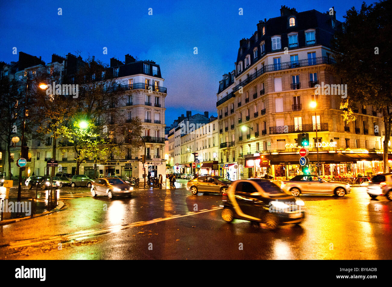 Place General Gouraud Wet Street Abenddämmerung Paris France // PARIS, Frankreich — Place Général Gouraud im 7. Arrondissement von Paris zeigt nasse Straßen in der Abenddämmerung. Der regendurchlässige Bürgersteig reflektiert das warme Leuchten der Straßenlaternen und Schaufenster. Diese Beleuchtung unterstreicht die klassische Haussmannische Architektur der umliegenden Gebäude. Diese markanten Strukturen mit ihren Steinfassaden und Mansardendächern sind ein Kennzeichen der Stadterneuerung von Baron Haussmann aus dem 19. Jahrhundert. Das 7. Arrondissement ist ein prestigeträchtiges zentrales Viertel, das für seine elegante Wohngegend bekannt ist Stockfoto