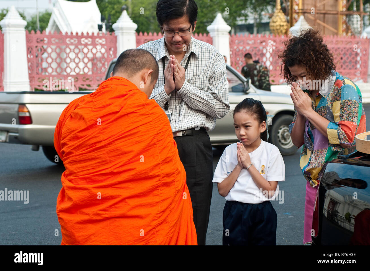 Eine Familie betet vor einem Mönch nach Almosen, Wat Benjamabophit, Bangkok, Thailand Stockfoto
