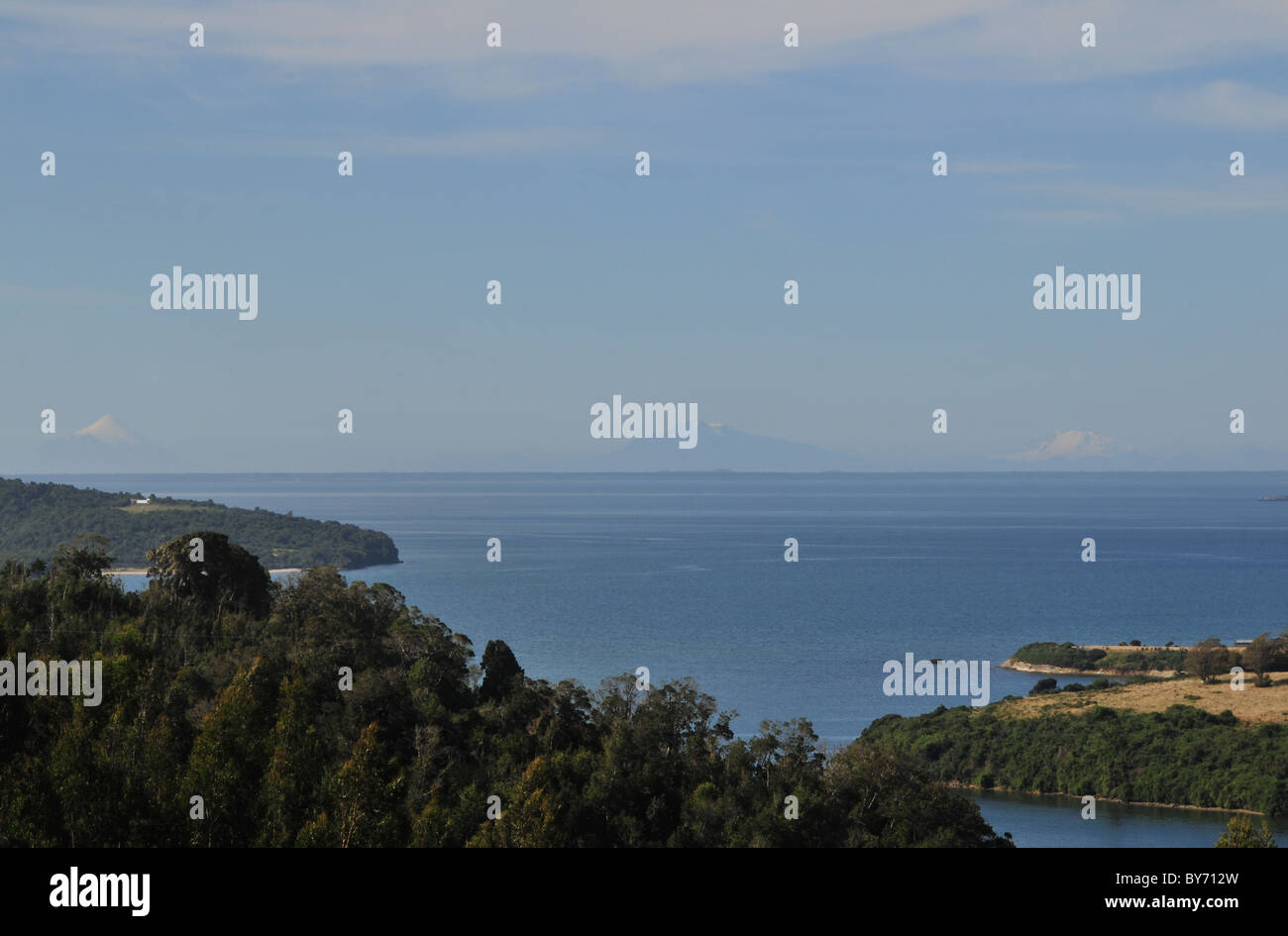 Blauer Himmel Bäume und Felder Blick auf den Golf von Ancud und fernen Osorno, Calbuco und Tronador Vulkane, Chiloé Insel, Chile Stockfoto
