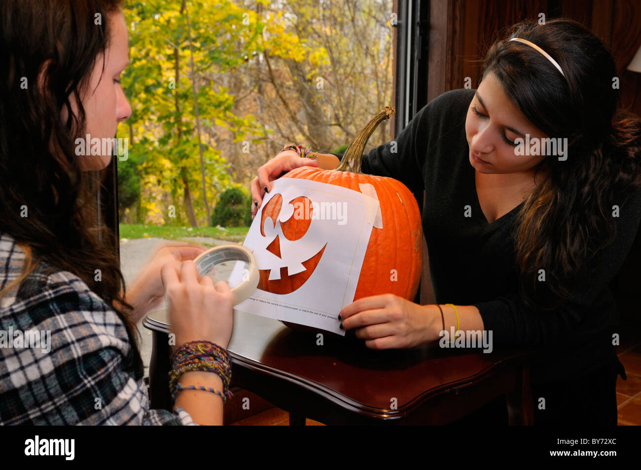 Zwei Mädchen im Teenageralter Anwendung eine Schablone mit einem Gesicht auf einem Kürbis für eine Halloween Jack O Lantern schnitzen Stockfoto