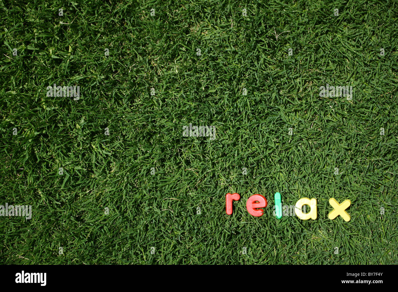 Das Wort "relax" dargelegt in bunten Buchstaben aus Kunststoff, auf dem grünen Rasen, genommen aus einem niedrigen Winkel Stockfoto