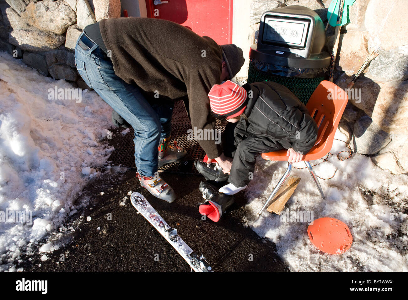 Vater seinen Sohn entfernen Skischuh zu helfen Stockfoto