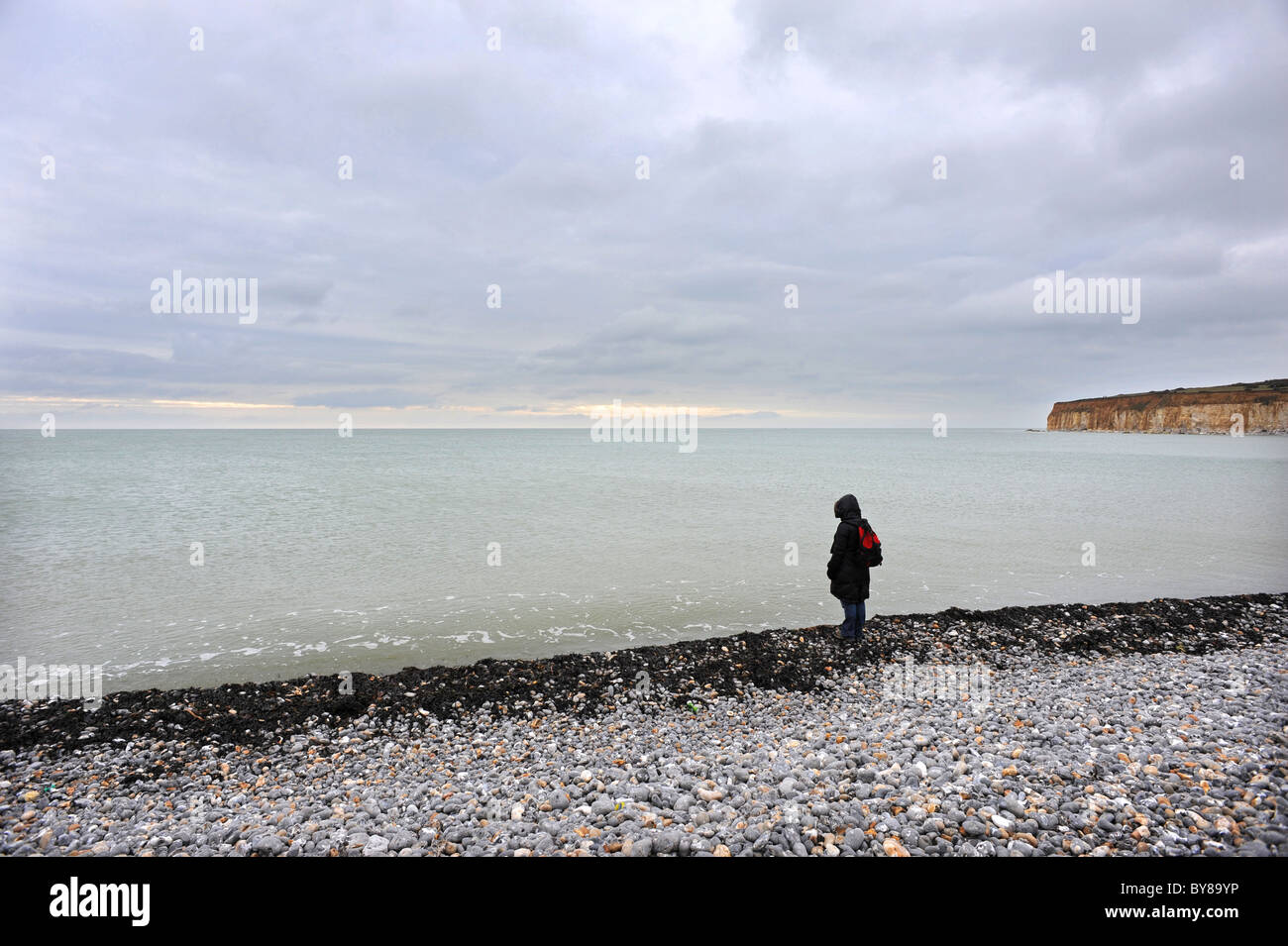 Eine einsame Gestalt blickt auf das Meer am Strand von Cuckmere Haven Stockfoto