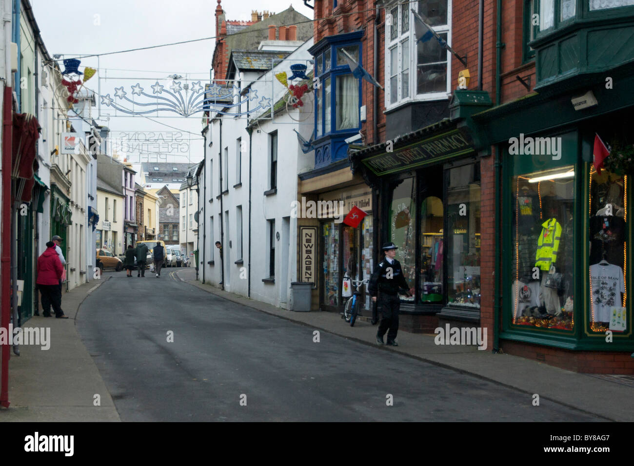 Micheal Street, Peel, Isle Of Man mit Weihnachtsschmuck und eine Polizistin zu Fuß in Richtung Kamera Stockfoto