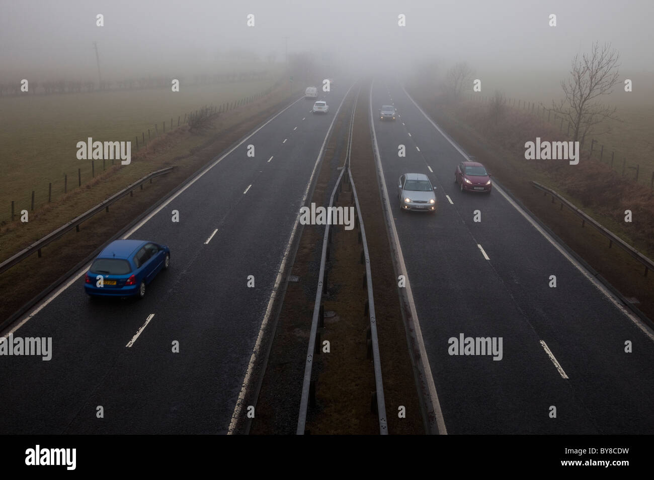 Fahrzeuge fahren entlang einer Autobahn an einem nebeligen Tag entlang. Die Sicht ist so gering, dass sie ihre Scheinwerfer eingeschaltet haben. Stockfoto