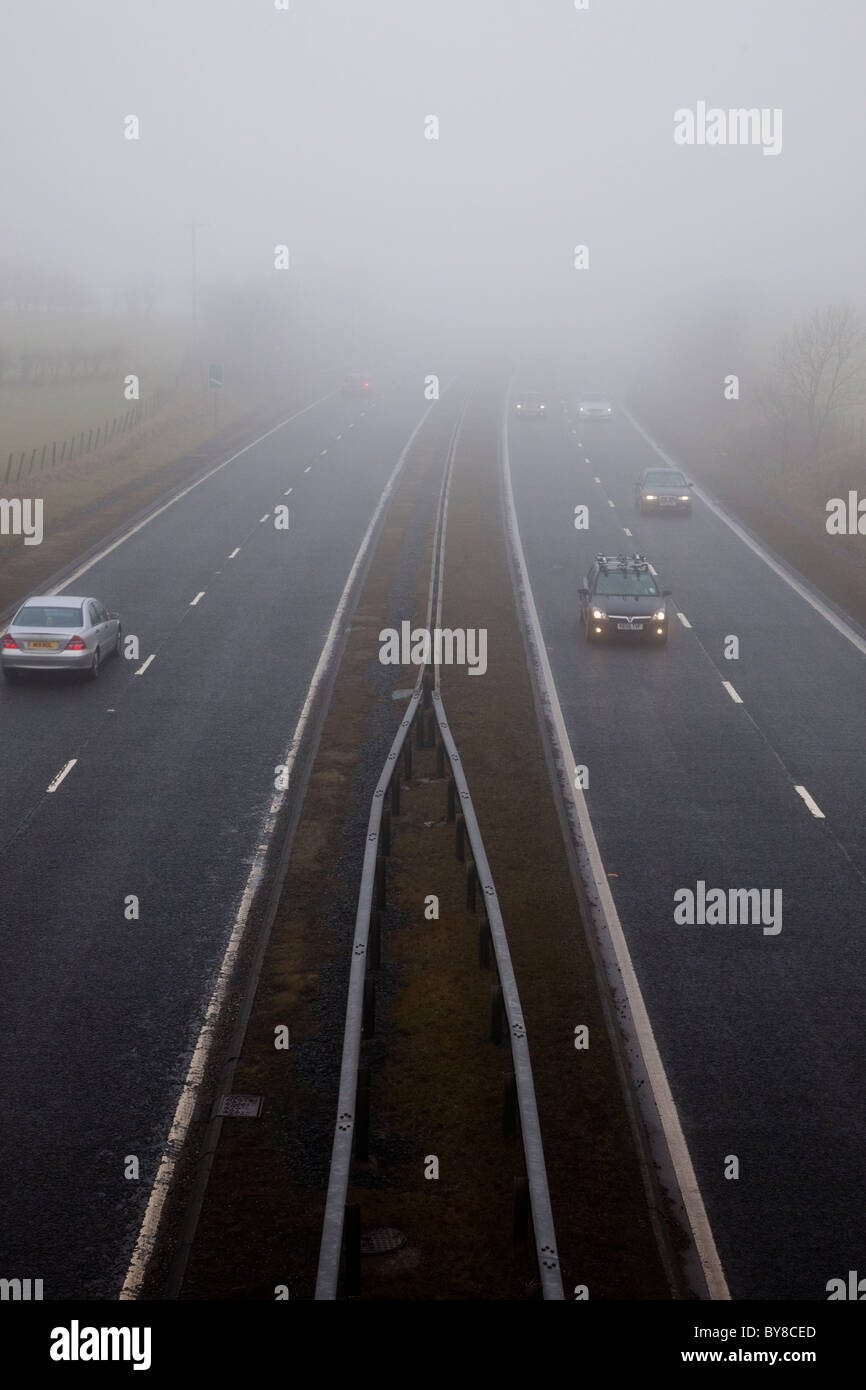 Fahrzeuge fahren entlang einer Autobahn an einem nebeligen Tag entlang. Die Sicht ist so gering, dass sie ihre Scheinwerfer eingeschaltet haben. Stockfoto