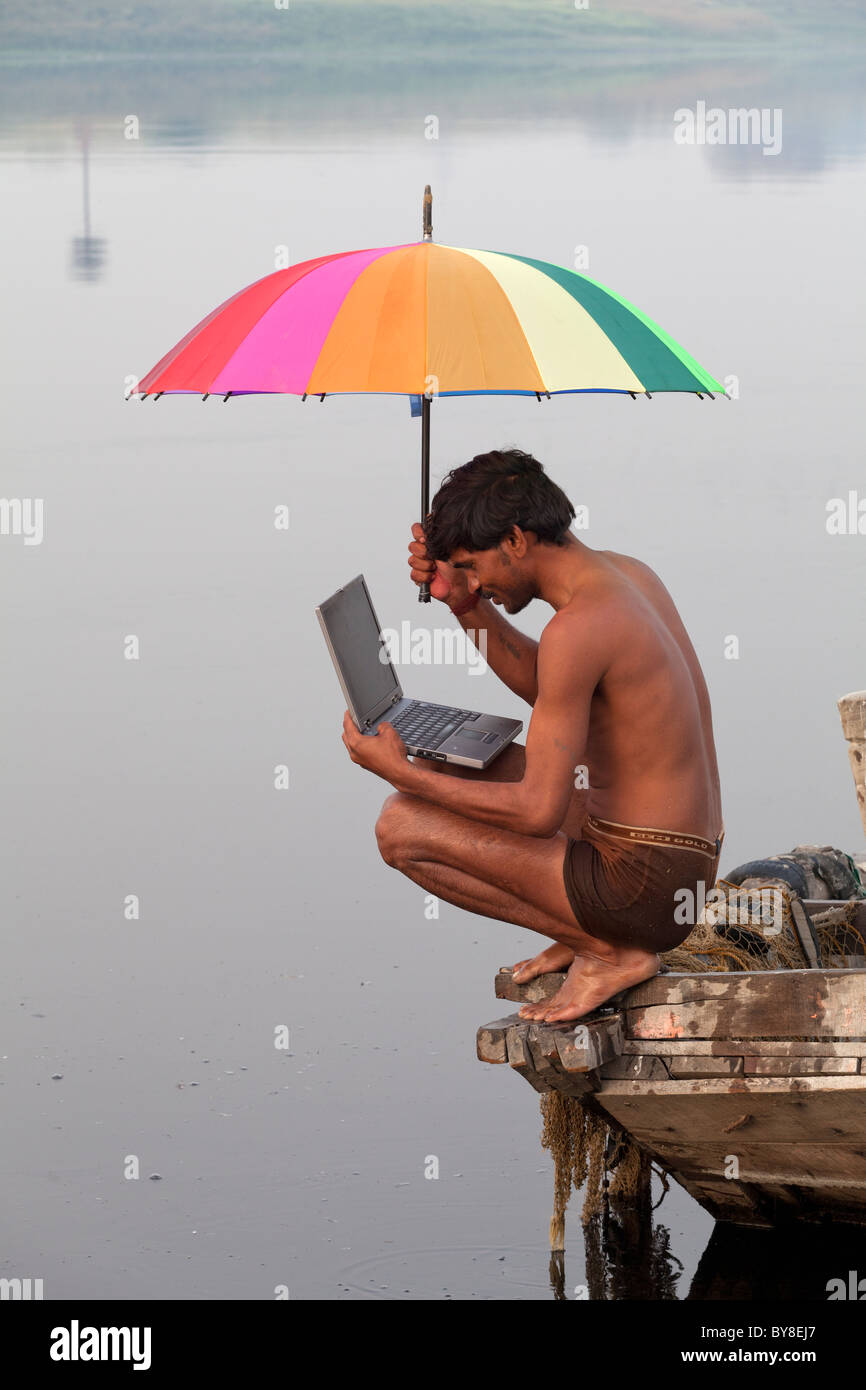 Indien, Agra, Uttar Pradesh Fischer am Boot bunten Regenschirm hält und mit Blick auf einen laptop Stockfoto