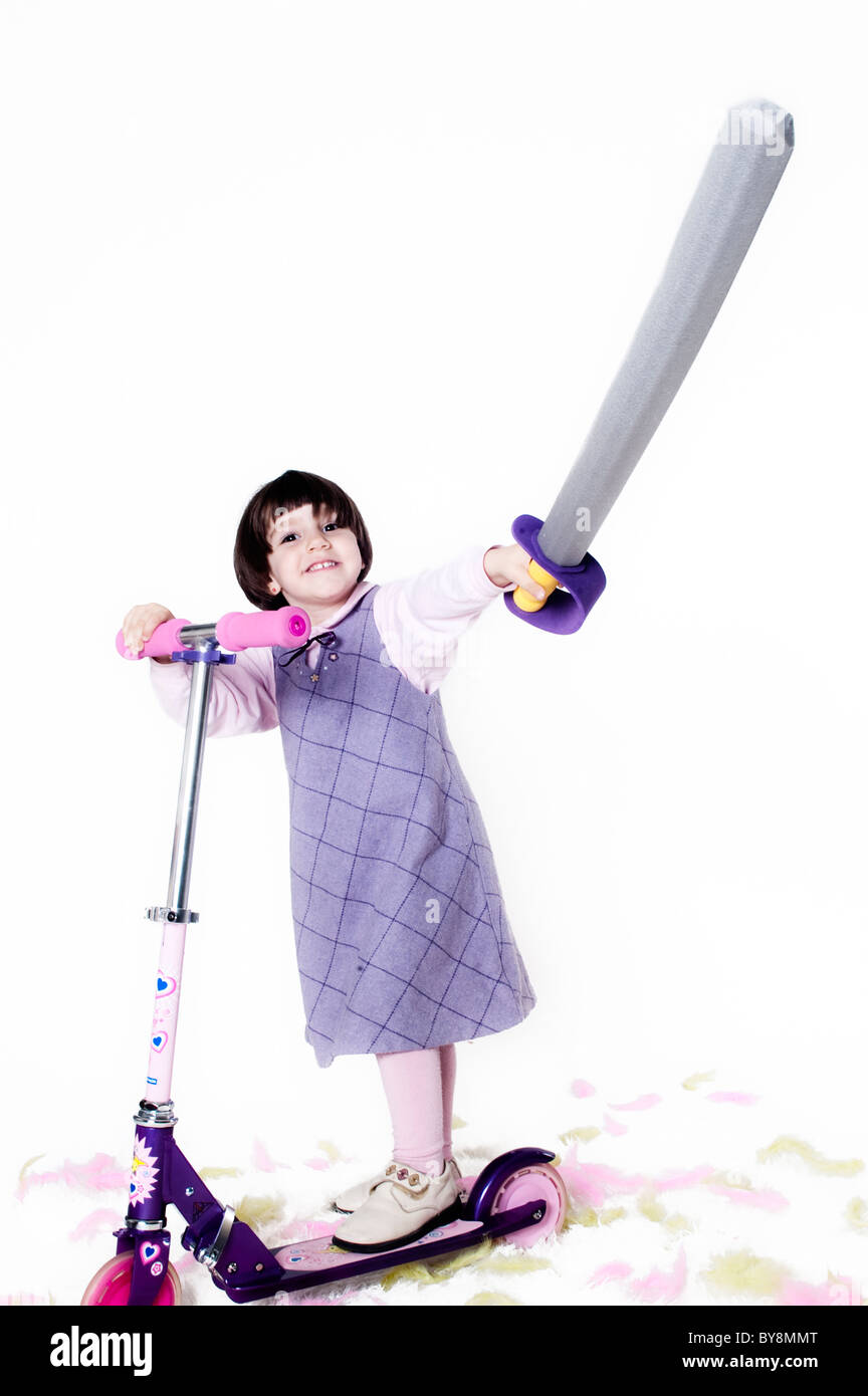 Kleines Mädchen in ihrem Roller und ein Spielzeug Schwert in seiner Hand hetzen Stockfoto