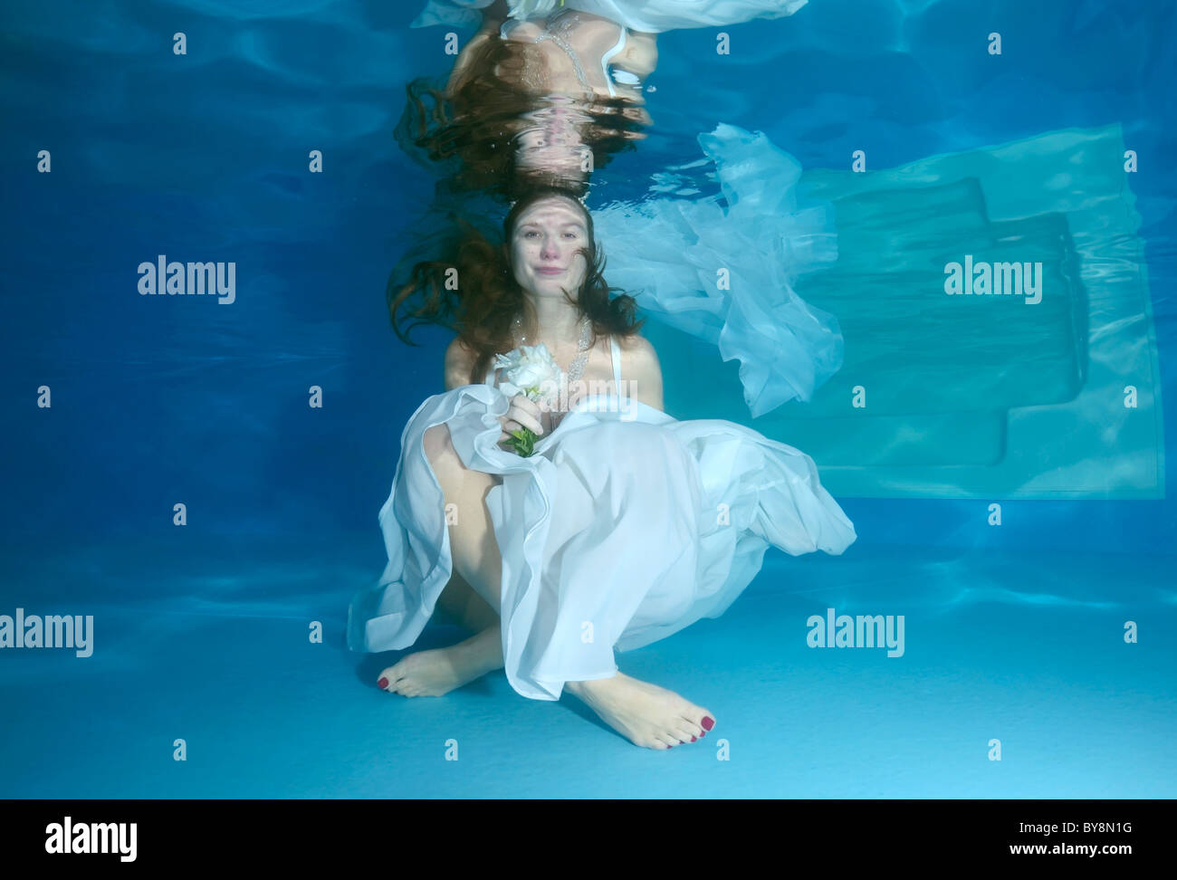 Eine junge Frau mit großen Haar posiert in einem Pool unter Wasser Stockfoto