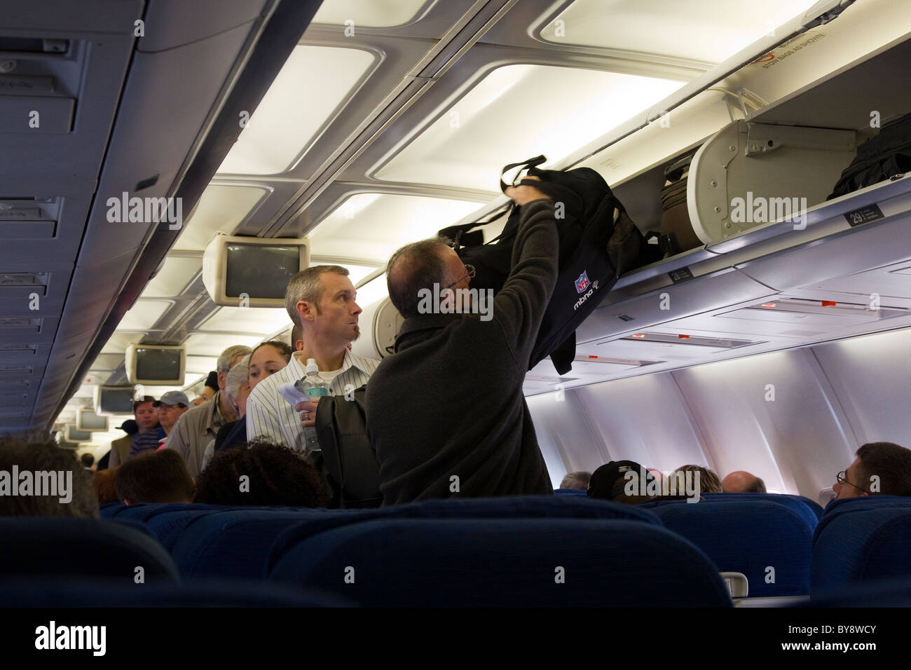 Passagiere vorbereiten für Flug, indem verstauen Handgepäck Gepäck im Gepäckfach in Flugzeug Stockfoto