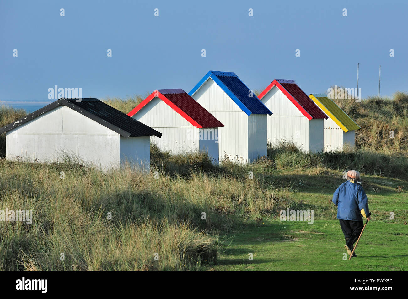 Frau zu Fuß vorbei an bunten Strandkabinen in den Dünen bei Gouville-Sur-Mer, Normandie, Frankreich Stockfoto