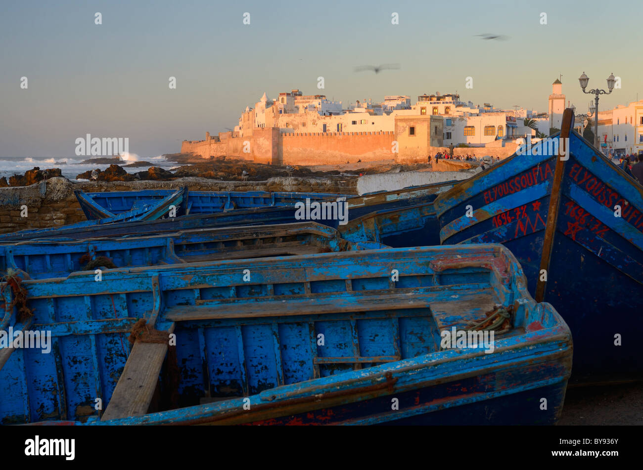 Blau Fischerboote und Atlantik surfen mit der Stadtmauer von Essaouira Marokko bei Sonnenuntergang Stockfoto