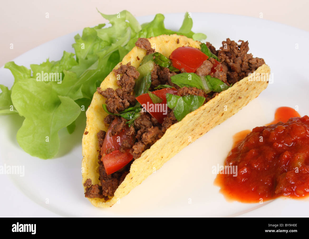 Ein Rind gefüllt Taco auf einem Teller mit Salsa und ein Salatblatt. Stockfoto