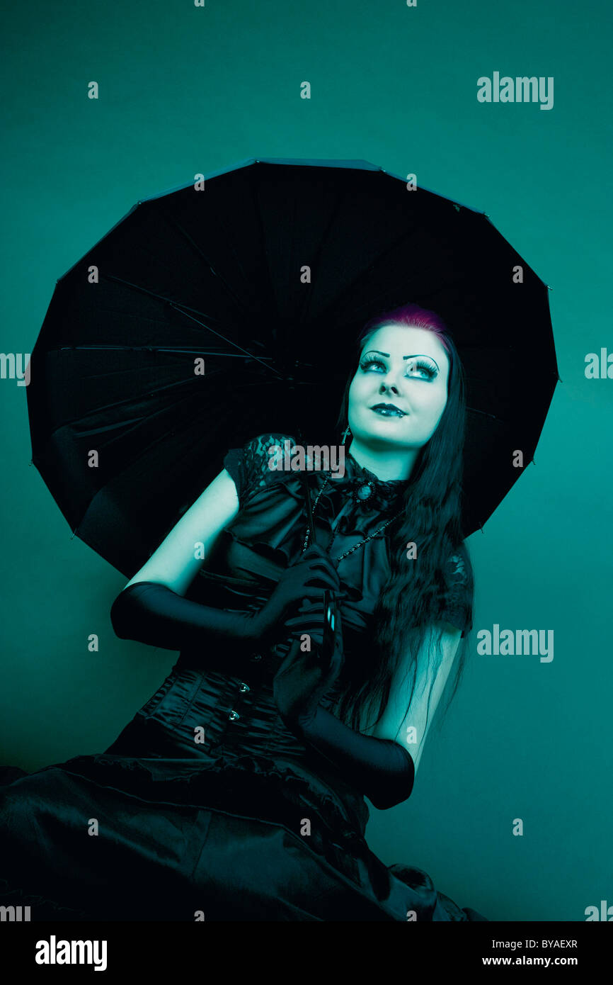Frau, Goth Subkultur, sitzt, hält einen Regenschirm und nachdenklichen Blick Stockfoto