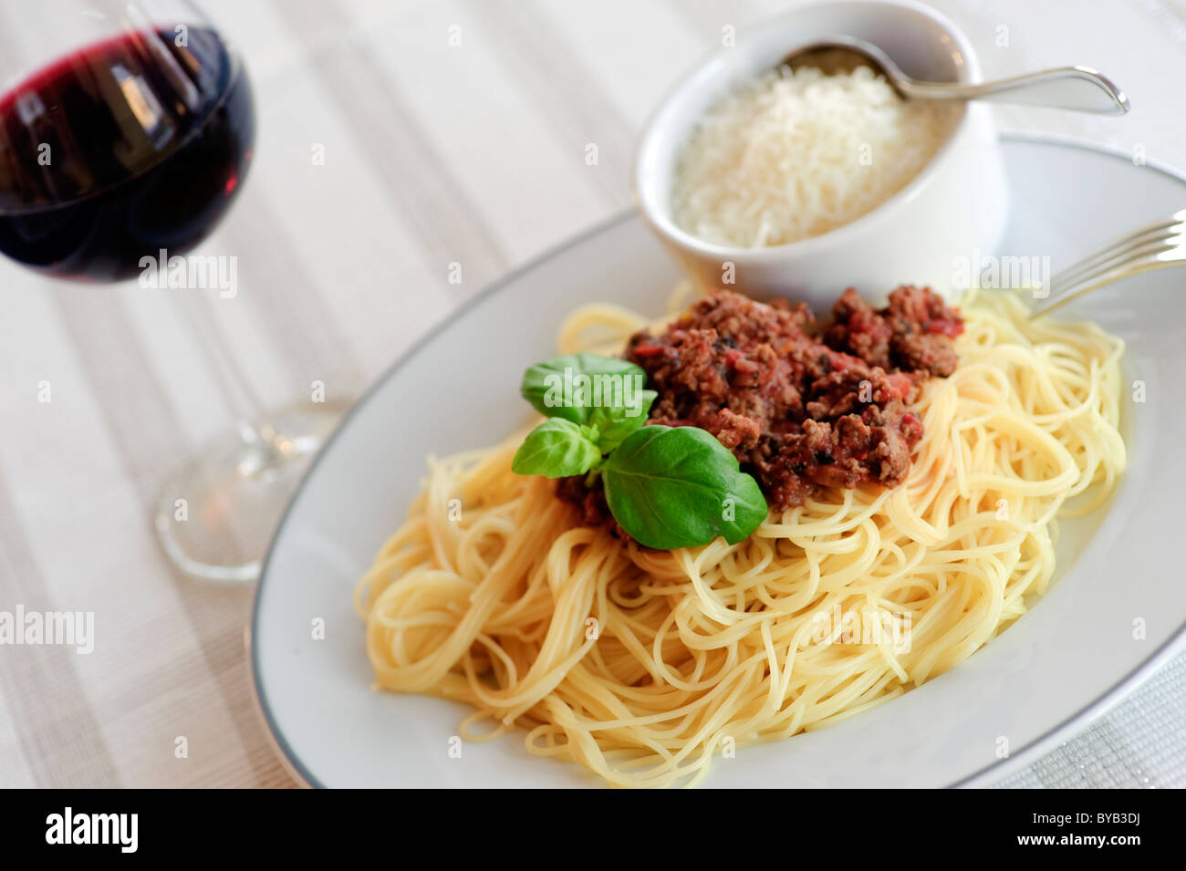 Einen Teller mit Spaghetti Bolognese, geriebenen Parmesan und ein Glas  Rotwein auf dem weißen Tischtuch Stockfotografie - Alamy