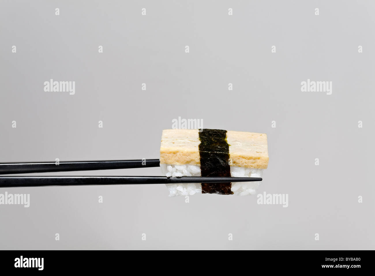 Schwarzen Stäbchen halten Nigiri Sushi mit Tofu, mit Nori umwickelt Stockfoto