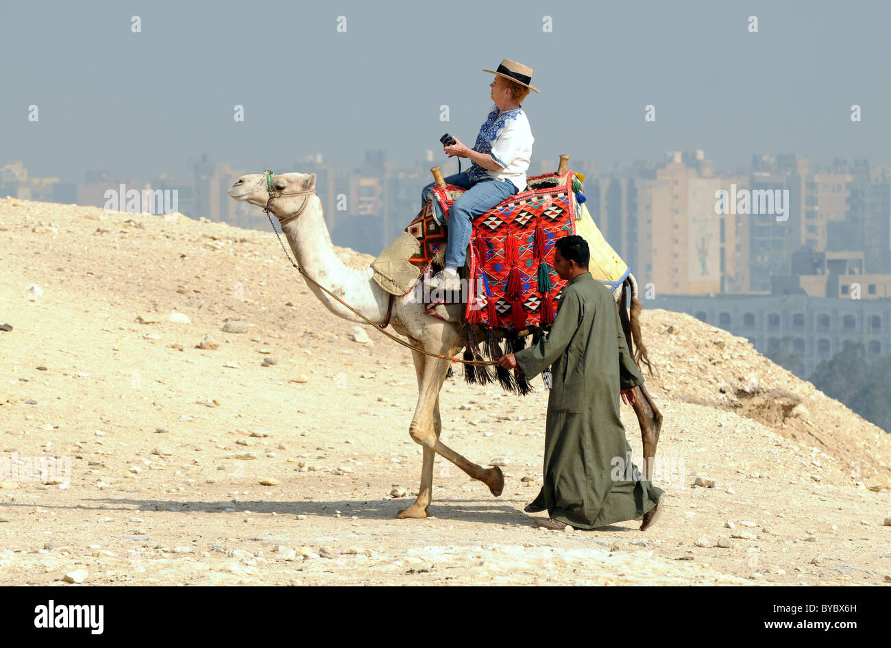 Ägypten, Touristen, Kamelreiten in Gizeh in Ägypten Cairo Stadt im Hintergrund. Stockfoto
