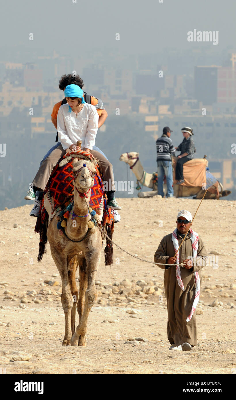 Ägypten, Touristen, Kamelreiten in Gizeh in Ägypten Cairo Stadt im Hintergrund. Stockfoto