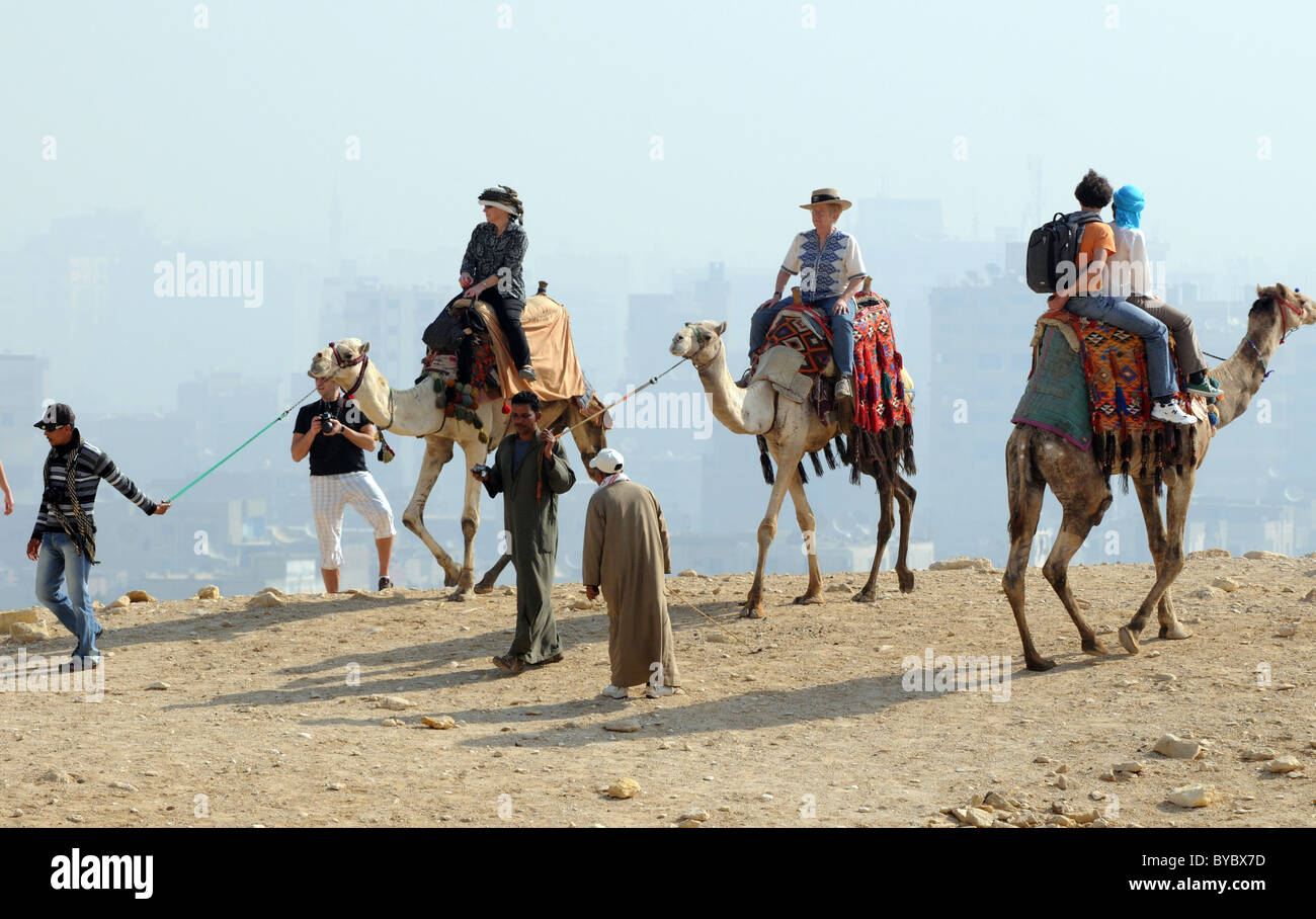 Ägypten, Touristen, Kamelreiten in Gizeh in Ägypten Cairo Stadt im Hintergrund. Stockfoto