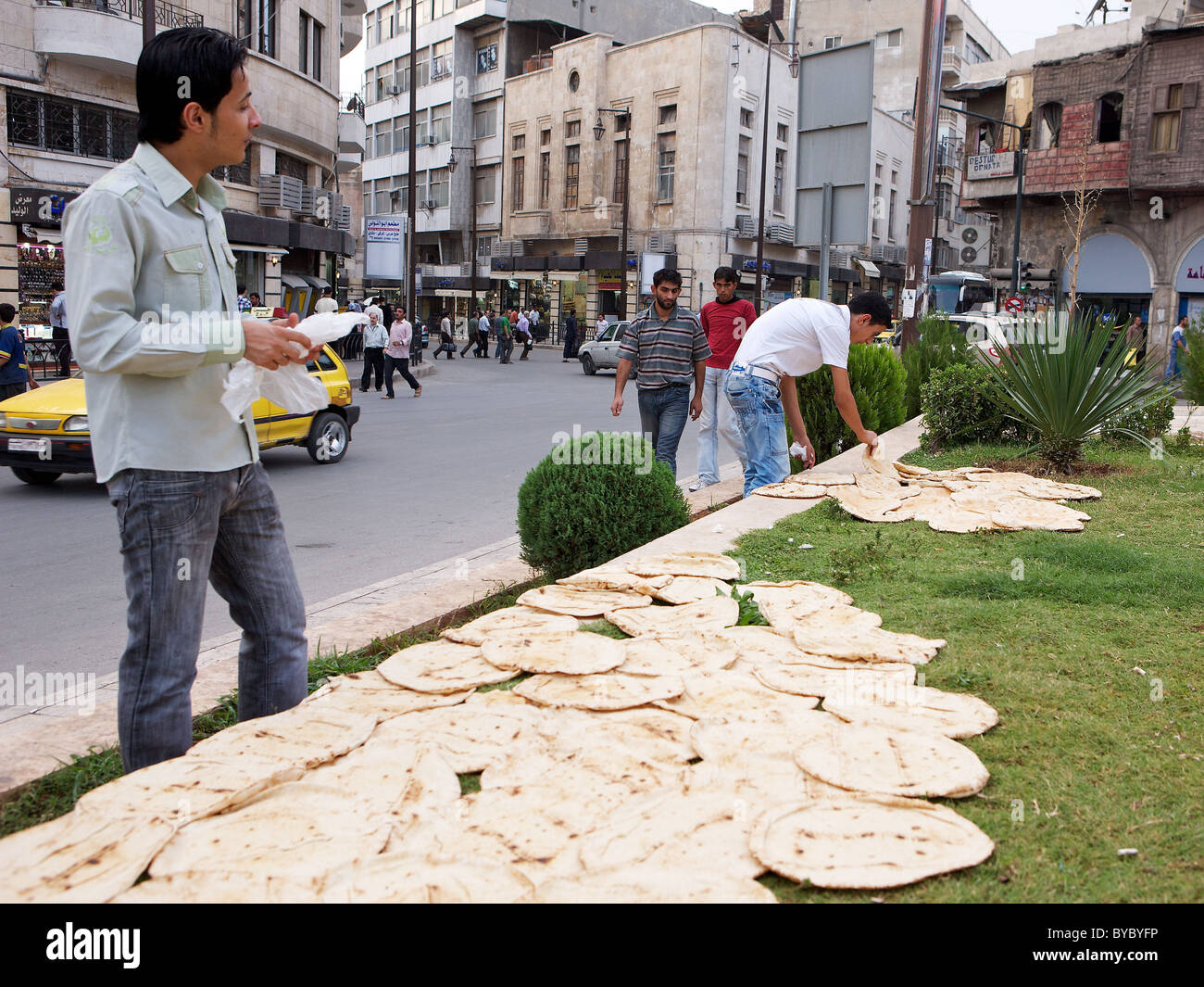 Syrische Männer trocknen ihr frisch gebackenes Brot auf dem Rasen auf der anderen Straßenseite von einer Bäckerei im Zentrum von Aleppo, Syrien Stockfoto
