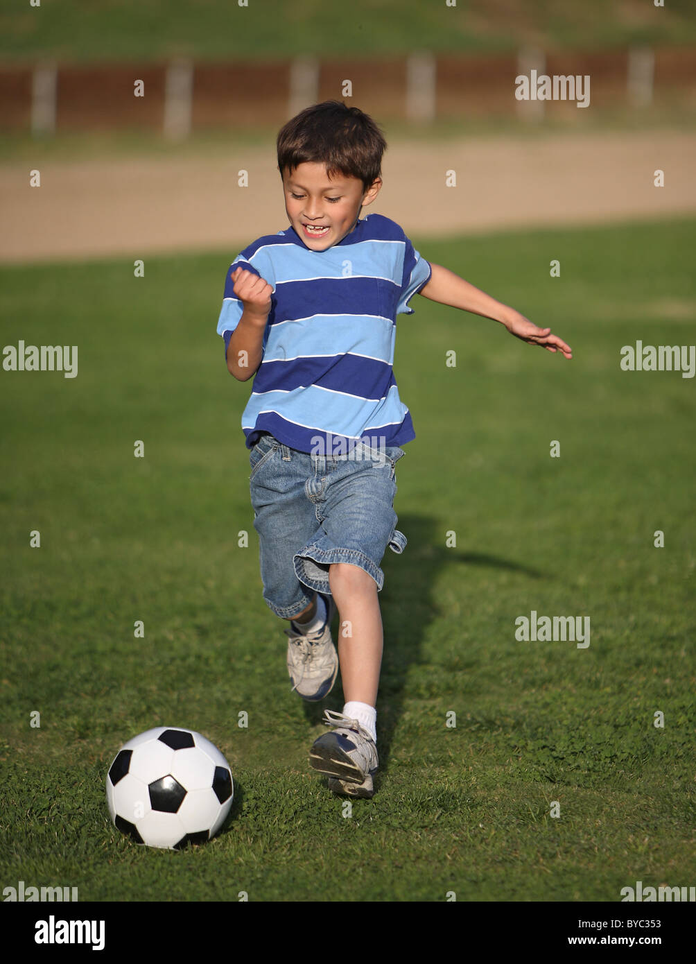 Authentische glücklich Latino Boy spielt mit Fussball Ball im Feld tragen blau gestreiften t-Shirt. Stockfoto