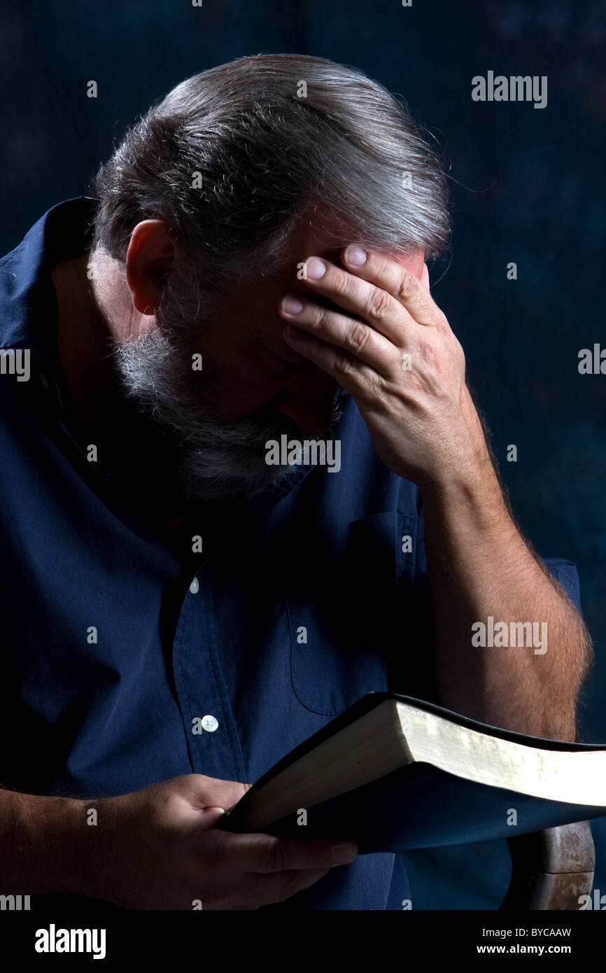 Mann hält seinen Kopf in einer Hand und neigt um zu beten, während seine Bibel in der anderen hält. Stockfoto