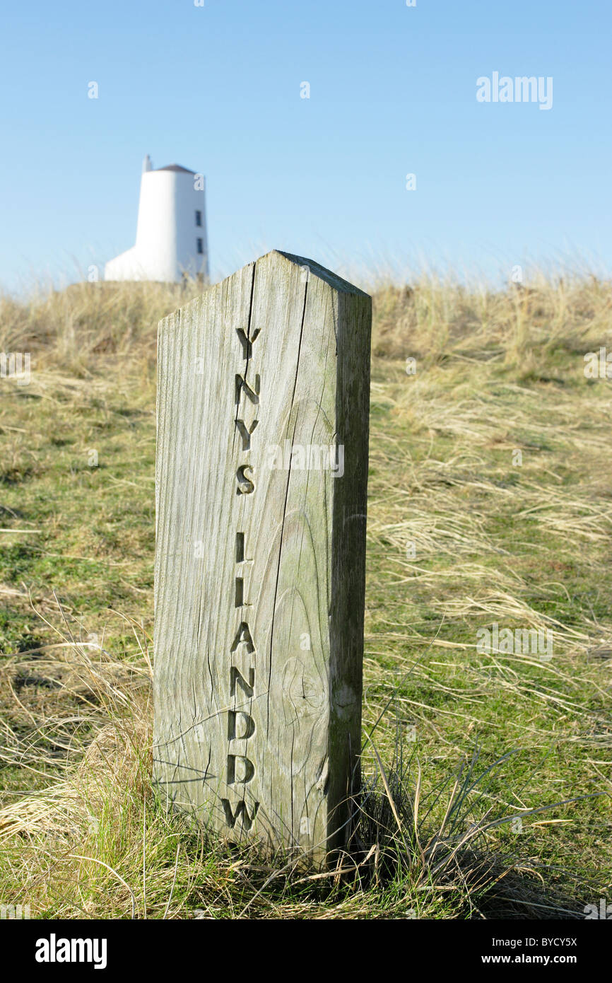 Ein Holzweg Marker Post auf Llanddwyn Island(Ynys Llanddwyn), Anglesey, Nordwales mit einem Leuchtturm im Hintergrund Stockfoto