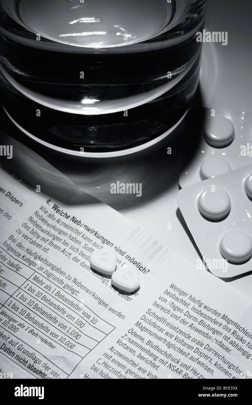 Tabletten auf ein Medikament-Paket legen Sie mit den entsprechenden Nebenwirkungen neben einem Glas Wasser Stockfoto