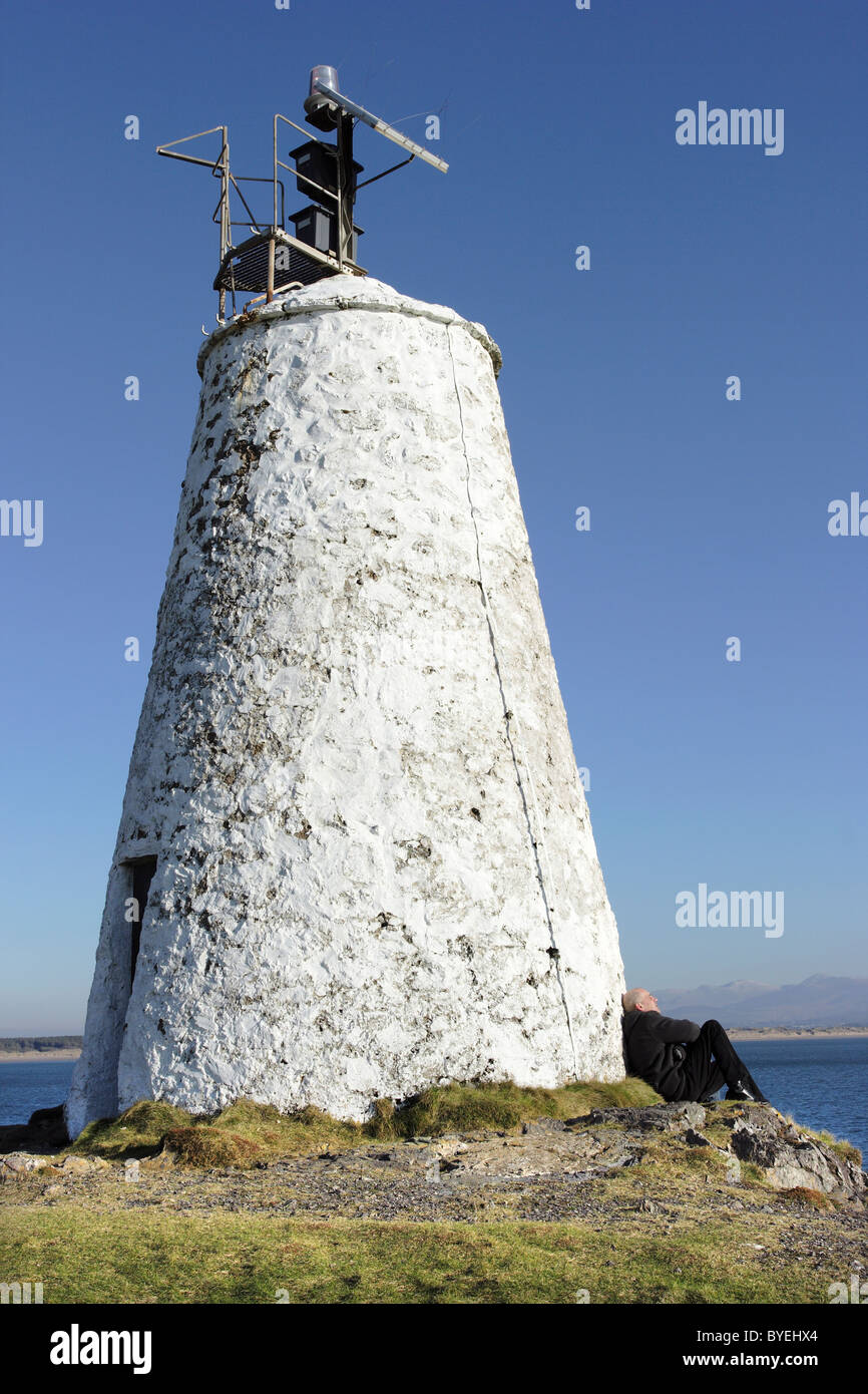 Ein Besucher ruht in der Sonne unter dem alten Leuchtturm auf Llanddwyn Island in Anglesey, die jetzt solarbetrieben Stockfoto