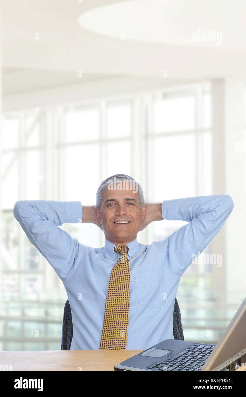Geschäftsmann sitzt an seinem Schreibtisch in ein modernes Bürogebäude mit Händen hinter dem Kopf. Stockfoto