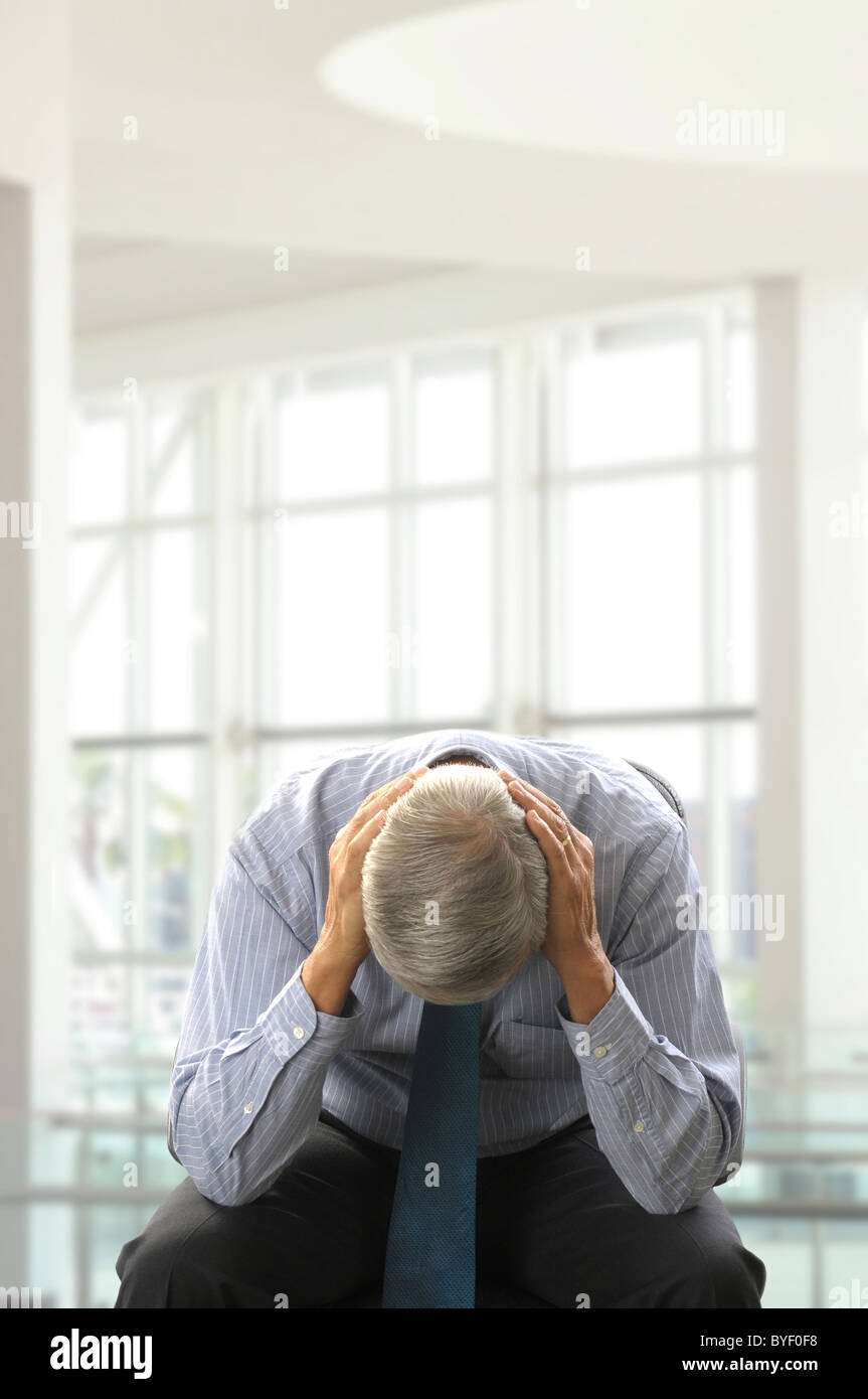 Mittleren Alter Geschäftsmann verdoppelt über mit seinem Kopf in Händen in einem modernen Business Büro sitzen. Stockfoto
