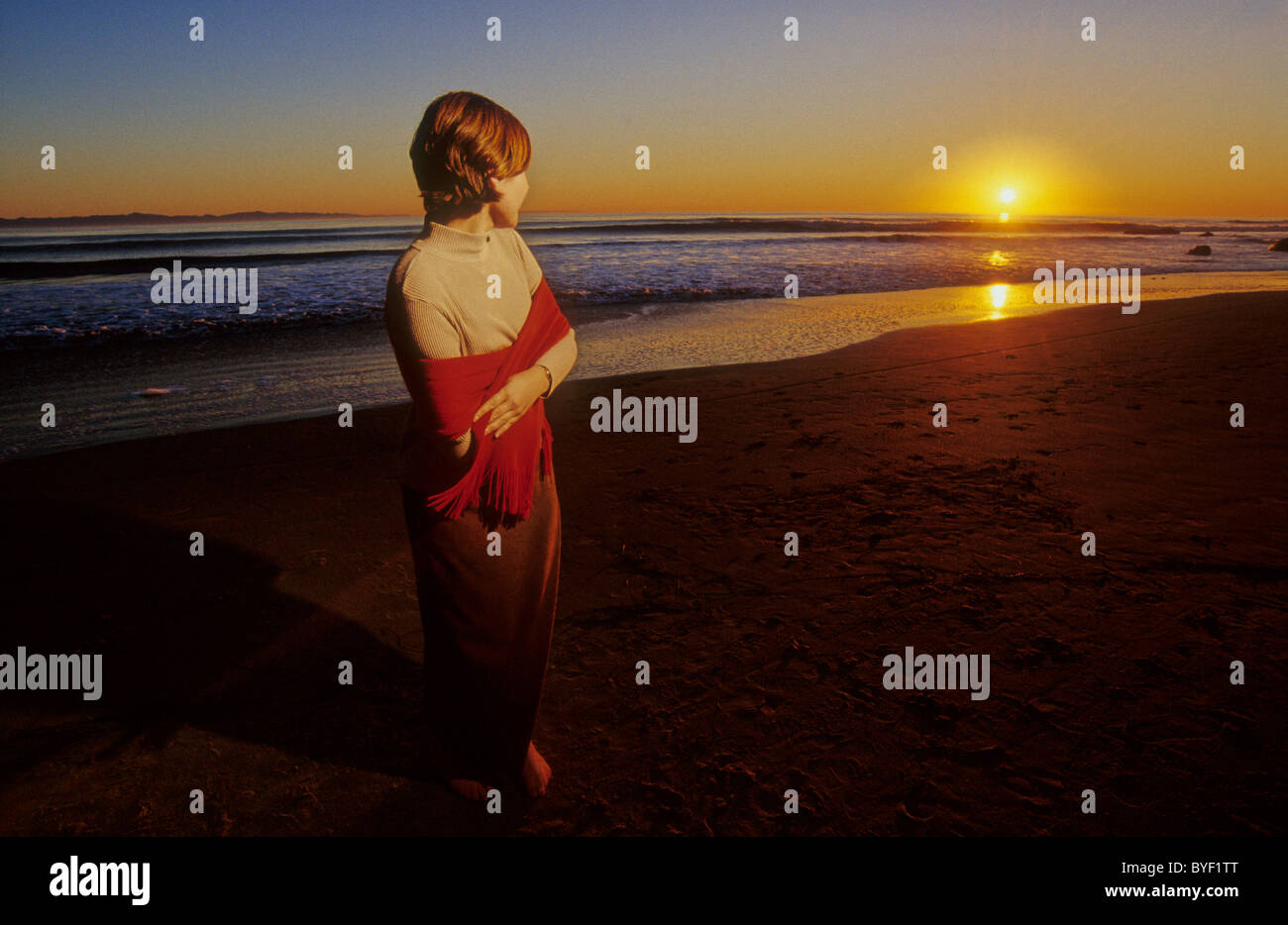 Frau am Strand bei Sonnenuntergang in Tuch gewickelt. Stockfoto