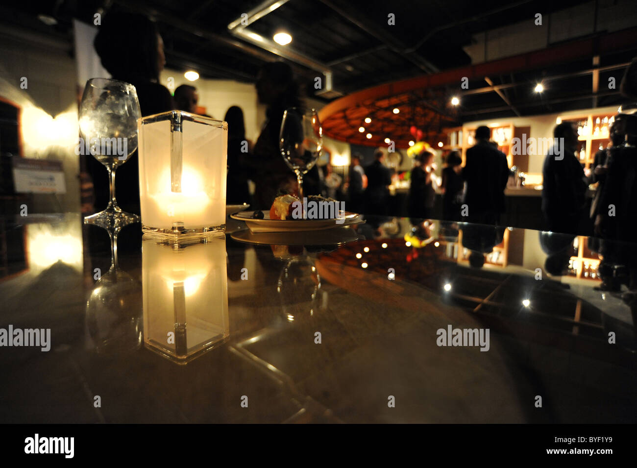 Eine Kerze spiegelt sich in einer Tischplatte auf einer Cocktailparty. Silhouetten von nicht identifizierbaren Partygänger im Hintergrund. Stockfoto
