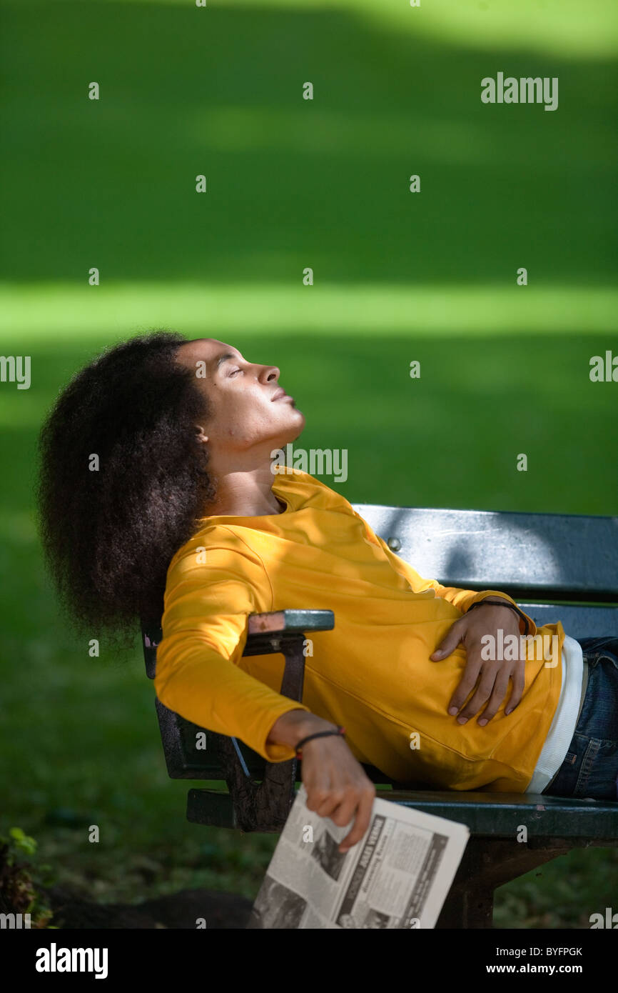 Junger Mann mit Afro-Haar entspannend auf Bank Stockfoto
