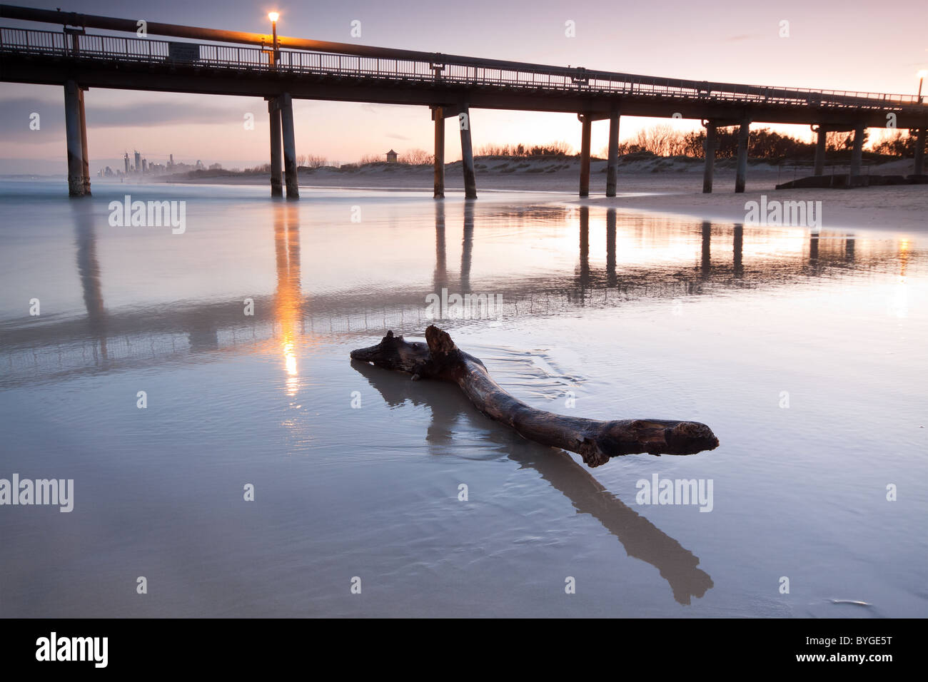 Melden Sie sich am Strand in der Abenddämmerung mit Steg und die Stadt im Hintergrund Stockfoto